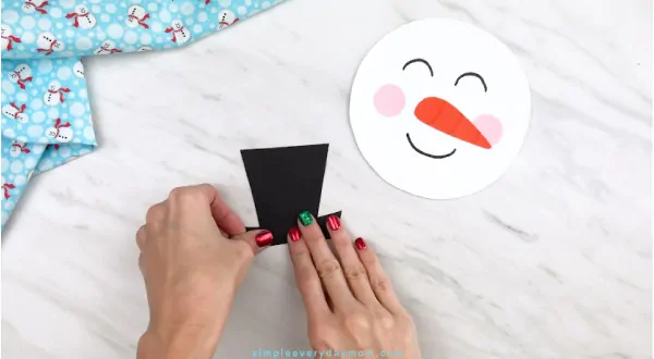 Hands gluing together snowman hat 