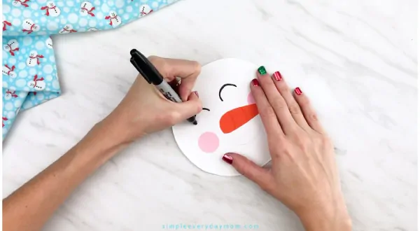 Hands drawing snowman eyes onto paper plate snowman 