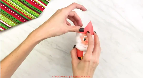 Hands gluing hat to toilet paper roll Santa craft