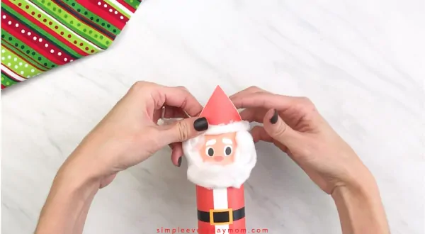 Hands gluing cotton ball fluff to Santa hat 