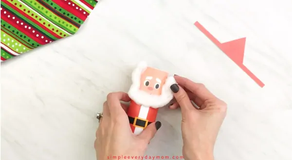 Hands gluing cotton bear to toilet paper roll Santa craft