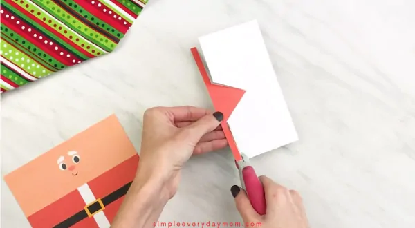 Hands cutting red paper Santa hat out 