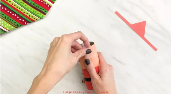 Hands taping toilet paper roll Santa craft onto tube 