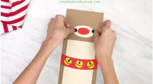 hand gluing nose onto paper bag reindeer craft
