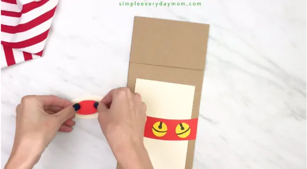 hands gluing paper nose onto muzzle for paper bag reindeer craft