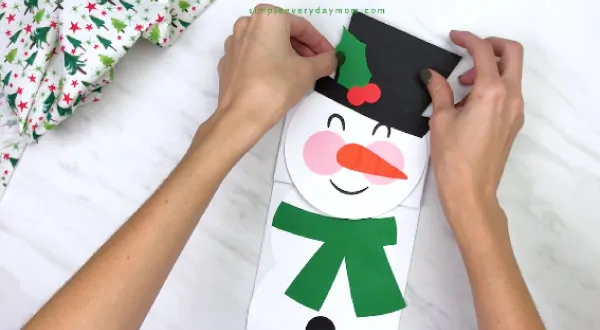 Hands gluing hat on paper bag snowman craft
