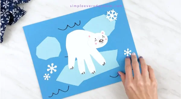 Hands gluing snowflake stickers onto polar bear craft 