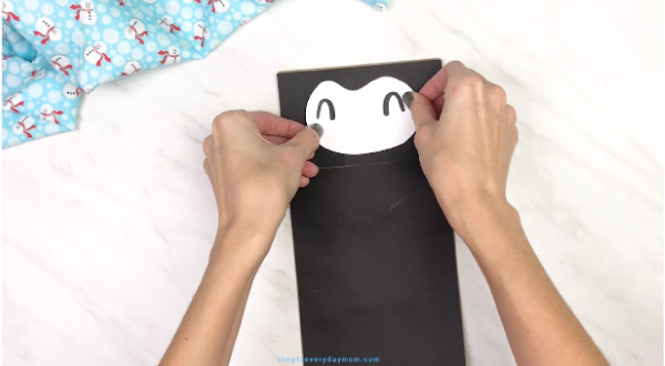 hands gluing face onto paper bag penguin craft
