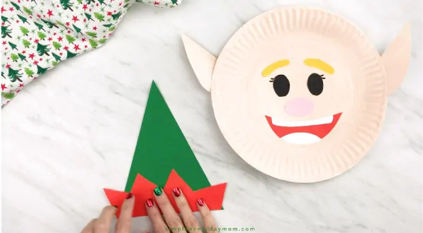 hands gluing elf hat together for paper plate elf craft
