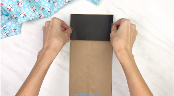 hands gluing black paper onto paper bag penguin craft