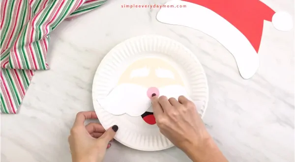 hands gluing nose onto paper plate Santa craft