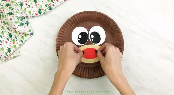 hand gluing nose onto paper plate reindeer craft 