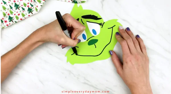 Hands drawing mouth onto grinch headband craft
