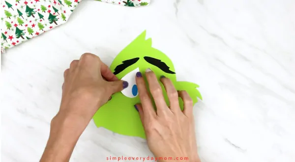 Hands gluing eyes onto grinch face 