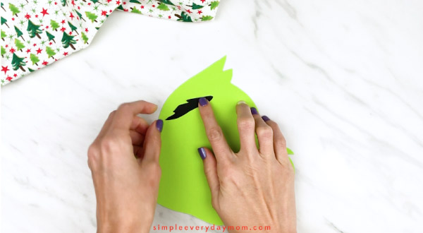 Hands gluing grinch eyes onto paper head 