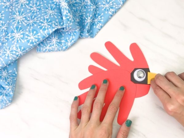 hands gluing beak onto handprint cardinal craft