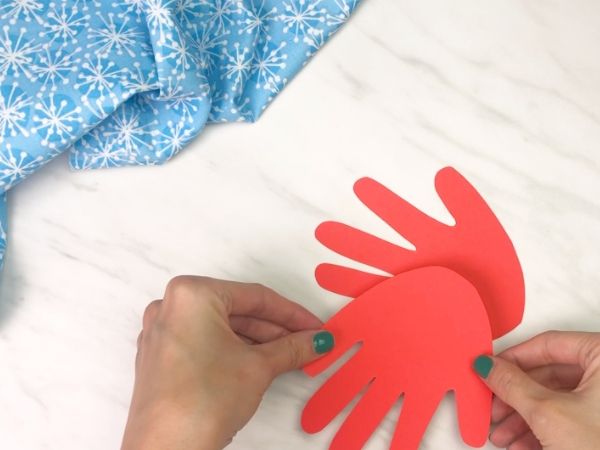 hands gluing red handprint together in the shape of a bird