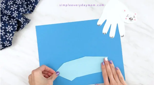 Hands gluing iceberg onto blue paper 