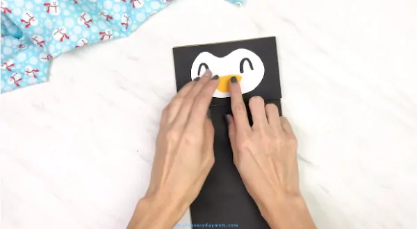 hands gluing beak onto paper bag penguin craft