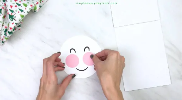 Hands gluing cheeks on paper bag snowman craft