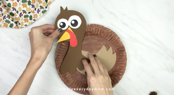 hands gluing feathers onto paper plate turkey craft