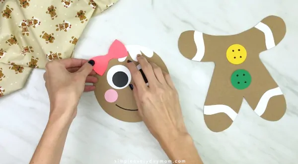 hand gluing bow to paper bag gingerbread craft