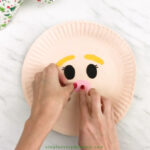 hands gluing nose onto paper plate elf craft