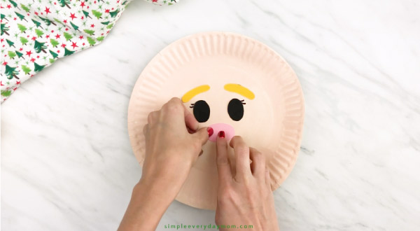 hands gluing nose onto paper plate elf craft