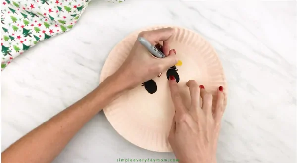 hands drawing eyelashes onto paper plate elf craft