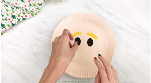 hands gluing eyes onto paper plate elf craft