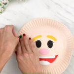 hands gluing ears onto paper plate elf craft