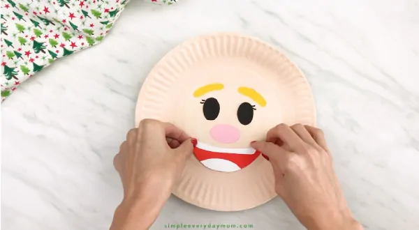 hands gluing mouth onto paper plate elf craft
