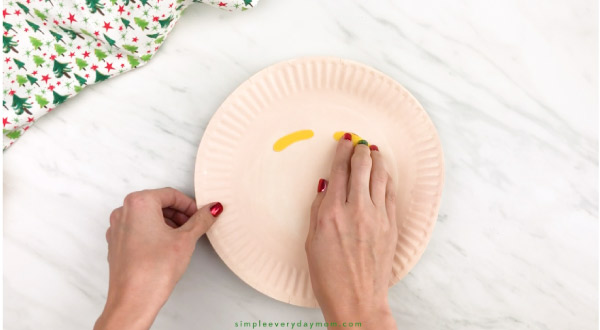 hands gluing eyebrows onto paper plate elf craft
