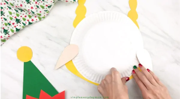 hands taping girl elf hair onto paper plate elf 