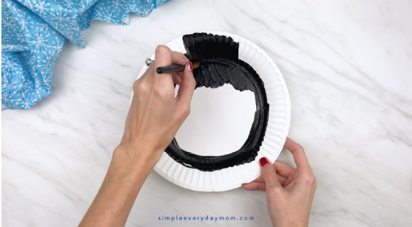 Hands painting paper plate black 
