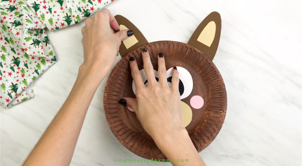 hand gluing ears onto paper plate reindeer craft 