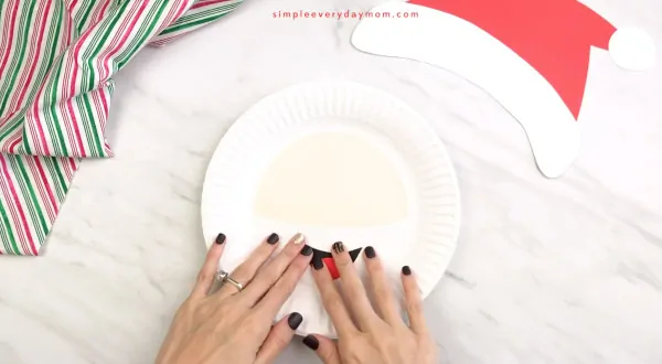hands gluing mouth onto Santa paper plate craft