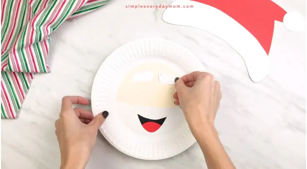hands gluing eyebrows onto Santa paper plate craft