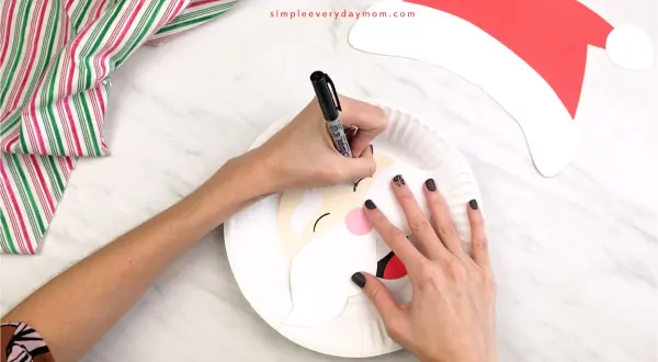 hands drawing eyes on paper plate Santa craft