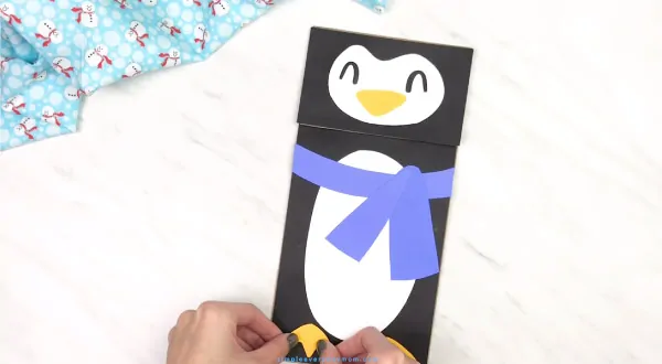 hands gluing feet onto paper bag penguin craft