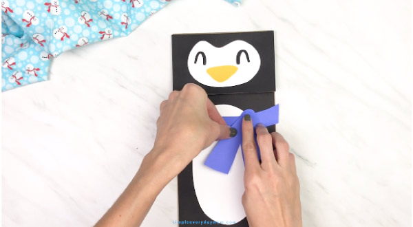 hands gluing scarf onto paper bag penguin craft
