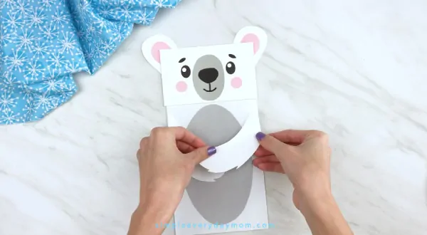 Hands gluing arms to paper bag polar bear craft 