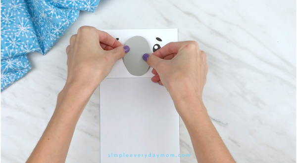 Hands gluing gray paper to polar bear craft 