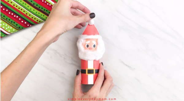 Hands gluing Santa hat puff to toilet paper roll Santa craft 