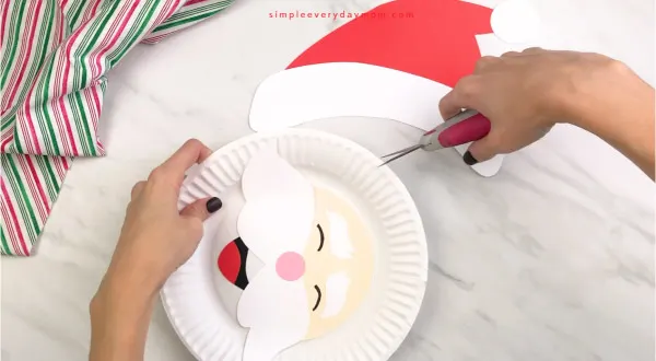 hands cutting slits into paper plate for paper plate santa craft