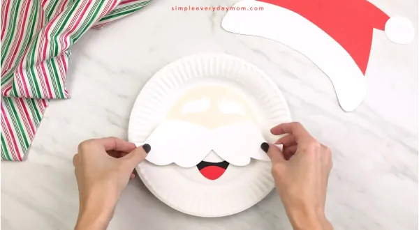 hands gluing mustache onto Santa paper plate craft