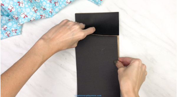 hands gluing black paper onto paper bag penguin craft