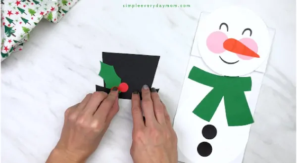 Hands gluing paper holly onto snowman hat 