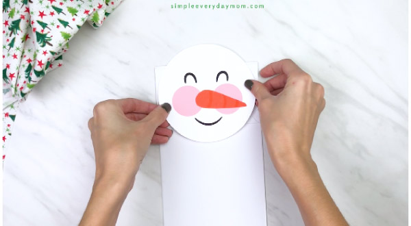 Hands gluing snowman face onto white paper bag 