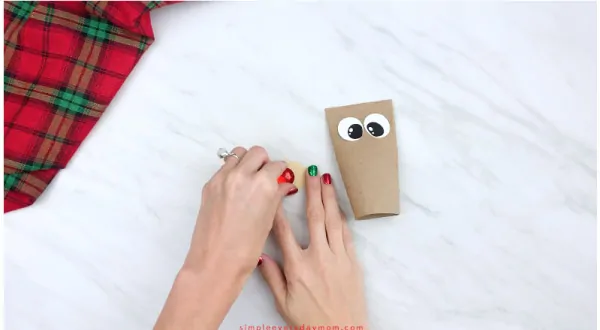 hands gluing red nose onto toilet paper roll reindeer muzzle 
